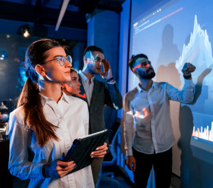 4 personas mirando una diapositiva con datos, dos hombre y dos mujeres, una de ellas usa camisa blanca y sostiene con ambas manos una tablet